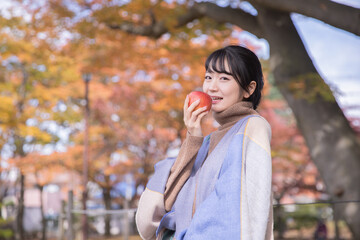 秋の公園でりんごを食べる女性
