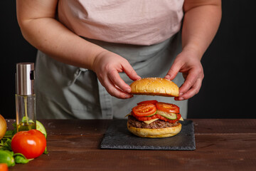 A close-up of a delicious burger being prepared. The cook sticks a skewer into the finished burger. Gastronomy, recipes, menus, fast food. Juicy burger