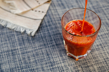 A thin stream of tomato juice fills the glass.