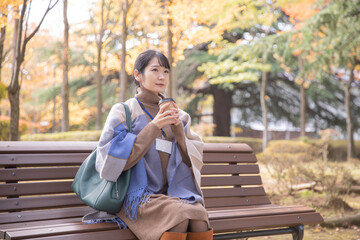 秋の公園でコーヒーを飲む会社員の女性（寒い）
