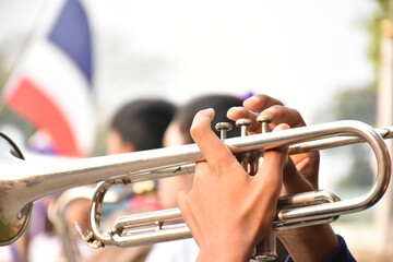 Trumpet instrument holding in hands of Asian student who playing it at a ceremony to honor the national flag in the morning. Soft and selective focus on trumpet.