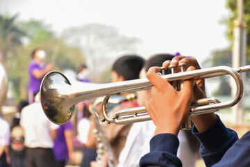 Fototapeta premium Trumpet instrument holding in hands of Asian student who playing it at a ceremony to honor the national flag in the morning. Soft and selective focus on trumpet.