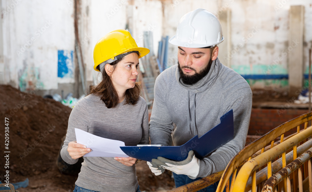 Wall mural two confident engineers discussing blueprint while standing at construction site