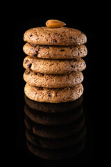 Oatmeal cookies with chocolate chips are isolated on a black background with a reflection. Lots of brown round homemade cookies lying on a reflective surface, close-up