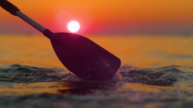 SLOW MOTION, CLOSE UP, LENS FLARE, SILHOUETTE, DOF: Gorgeous golden sunset shines on the kayaker's paddle splashing ocean water. Scenic shot of the endless Adriatic sea at sunrise and rower's paddle.