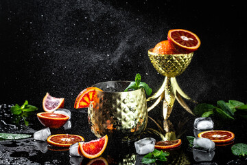 Moscow mule cocktail with blood orange, fresh mint leaves and ice in copper mugs, splashes and ice frozen motion