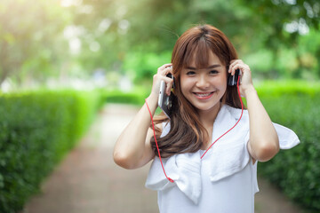 Happy smiling Asian woman wearing headphone using smartphone at the park. Looking at camera.