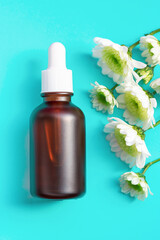 Bottle with serum and flower on blue background close-up.