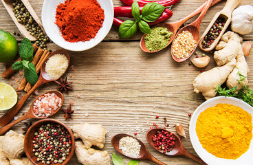 A selection of various colorful spices on a wooden table in bowls and spoons