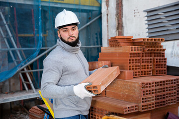 Obraz premium Serious young man working on his house renovations, stacking red bricks ..