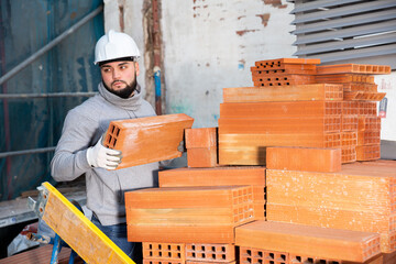Serious young man working on his house renovations, stacking red bricks ..