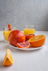Sweet and juicy blood oranges and oranges, whole and cut on a white plate and gkasses of fresh...
