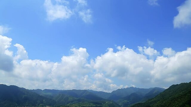 Green mountain and white clouds in blue sky, time-lapse of cloudscape