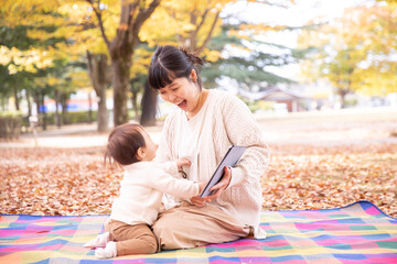 秋の公園でママとタブレットPCで遊ぶ赤ちゃん
