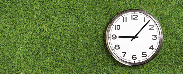 White plain analogue wall clock on green turf grass background. Five past nine oclock. copy space,...