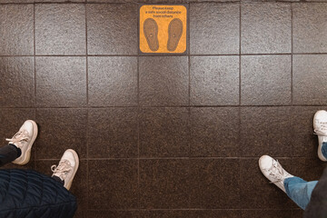 Keep social distance sign message on the ground, feet of two people. Shot from above, overhead