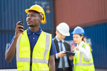 Smiling builder Engineering in hardhat with walkie talkie over group of builders at construction site..