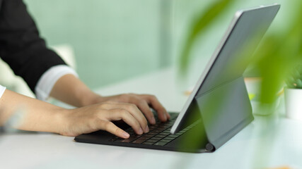 Female hands typing on tablet keyboard on white table decorated with plant pot