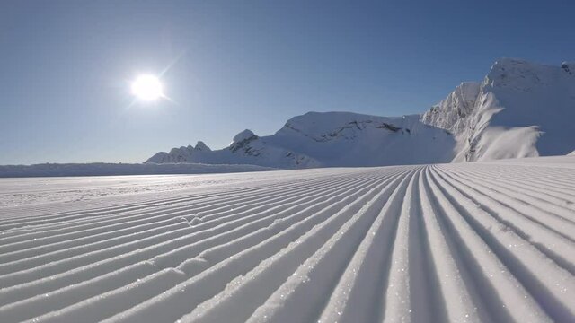 corduroy on the ski track after the snow-sealing machine in the early morning. the camera moves along the pristine corduroy against the backdrop of the mountain top and the bright sun in the blue sky