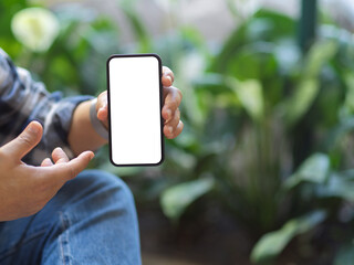 A man showing mock up smartphone screen to camera with blurred garden background