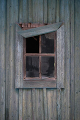 A small wooden window with broken glass and a rickety skirting board against the old wooden wall.