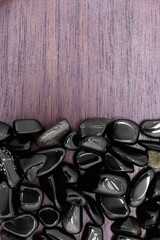 Gold obsidian rare jewel on half brown varnished wood texture. Pile mineral pebbles background....