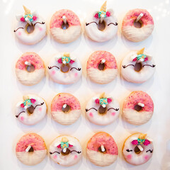 A set of donuts, row 4 by 4. Pink striped donuts and unicorn donuts hang on hooks in a checkerboard pattern on a white background. High quality photo