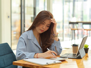 Businesswoman feeling stressed while working with financial paperwork and calculator