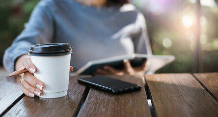Focus on hand of young asian female holding coffee cup while she reading book and relaxing outdoor cafe