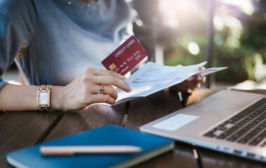 Close-up of hand asian businesswoman holding credit card and checking bank statement while she working with computer laptop outdoor