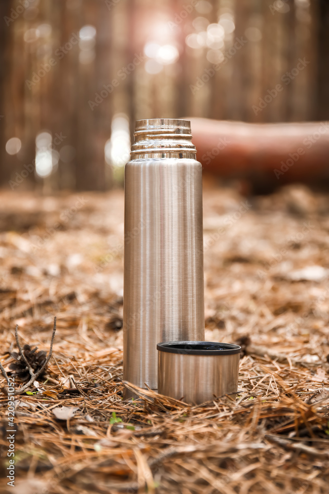 Wall mural Thermos with hot tea in forest