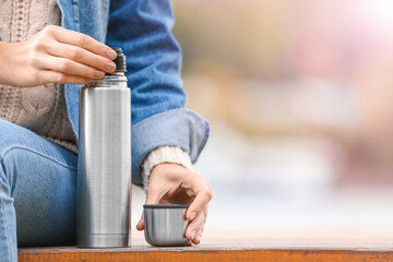 Young woman with thermos drinking hot tea outdoors