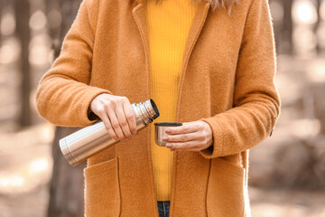 Female tourist with thermos drinking hot tea in forest