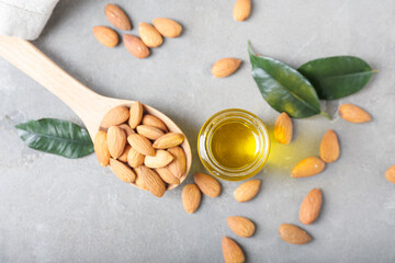 Jar with almond oil and spoon with nuts on grey background