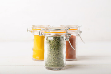 Jars with different spices on wooden table against white background