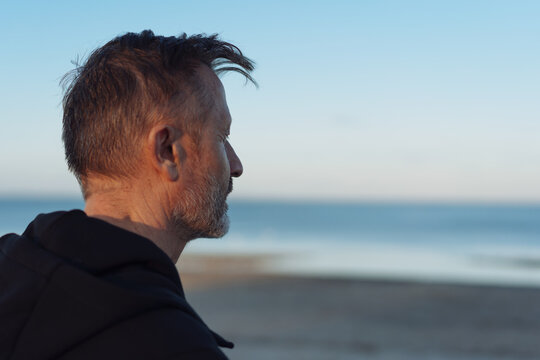 Bearded man standing staring out over the ocean at sunset