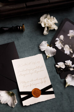 A set of wedding invitation cards and envelopes. Cards with calligraphy and flower petals on a dark background.