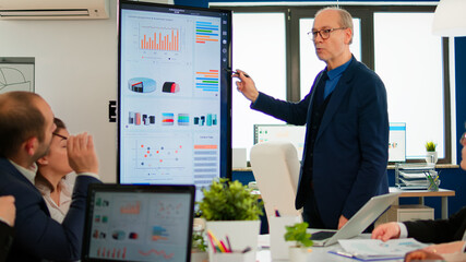 Mature CEO CTO executive director presenting statistical data, financial project briefing diverse group of employees. Multiethnical team working in professional startup company during conference