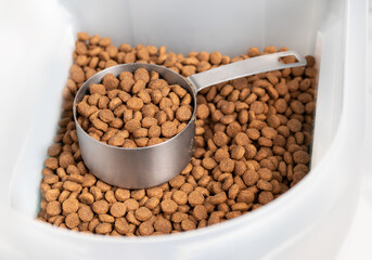 Kibbles with measuring cup inside larger food storage bucket. 1 cup dry pet or dog food portioned...