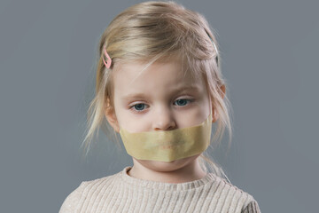 Studio portrait of adorable little girl with adhesive tape over her mouth. Little girl with no...