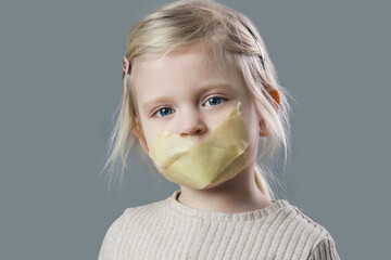 Studio portrait of adorable little girl with adhesive tape over her mouth. Little girl with no voice, freedom of speach or forbidden opinion concept.