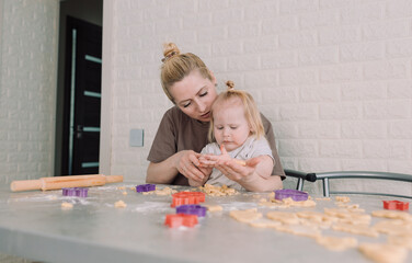 happy young mother and her little daughter together prepare delicious cookies sitting at the table...