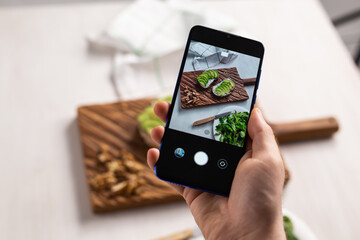 Hands take pictures on smartphone of two beautiful healthy sour cream and avocado sandwiches lying on board on the table. Social media and food concept