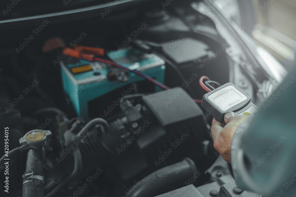 Poster selective focus an auto mechanic uses a multimeter voltmeter to check the voltage level in a car bat