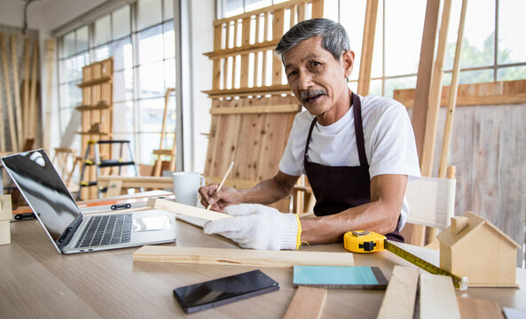 Senior Asian carpenter writing down data from laptop