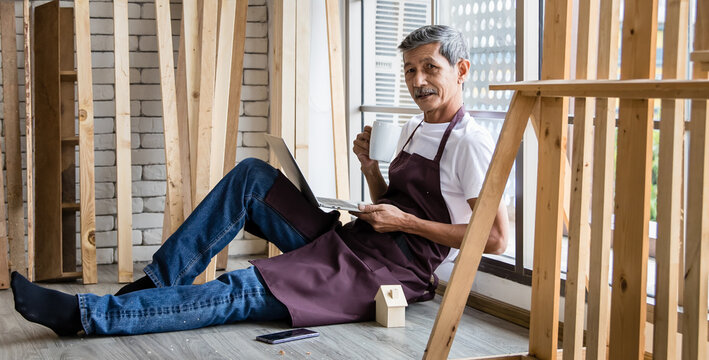 Senior Asian carpenter resting with laptop and drink