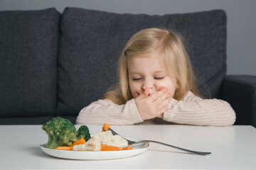 Toddler does not want to eat vegetable. Portrait of little girl refusing vegetable from plate in...