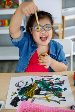 Asian girl with Down syndrome smiling and painting.