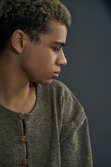 Staged photo illustrates problems and conflicts in gay couple relationships. Young swarthy man with far-away look is posing on the gray background.