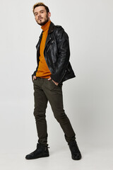 guy in an orange sweater holds his hands in his pants pockets black shoes leather jacket fashion style